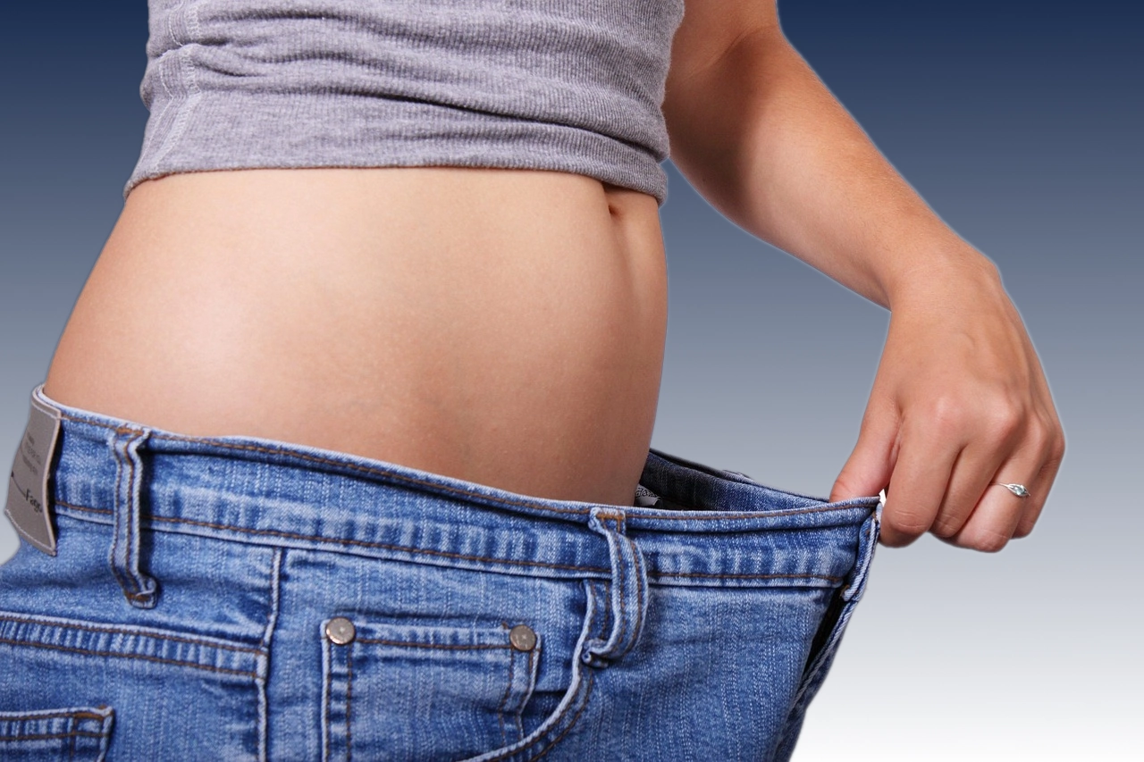 Femme tenant son pantalon devenu trop large après une perte de poids, symbole de transformation et de réussite