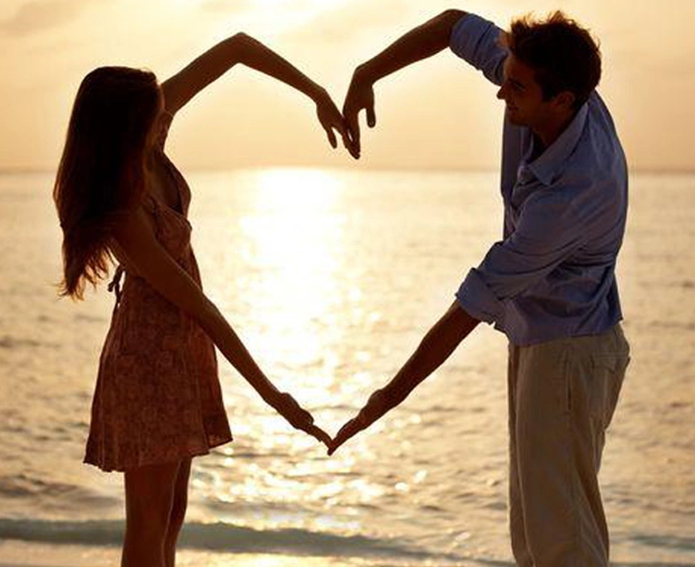 Couple formant un cœur avec leurs bras au bord de la mer, illustrant l’harmonie retrouvée grâce à une thérapie de couple dans le Lot (46)