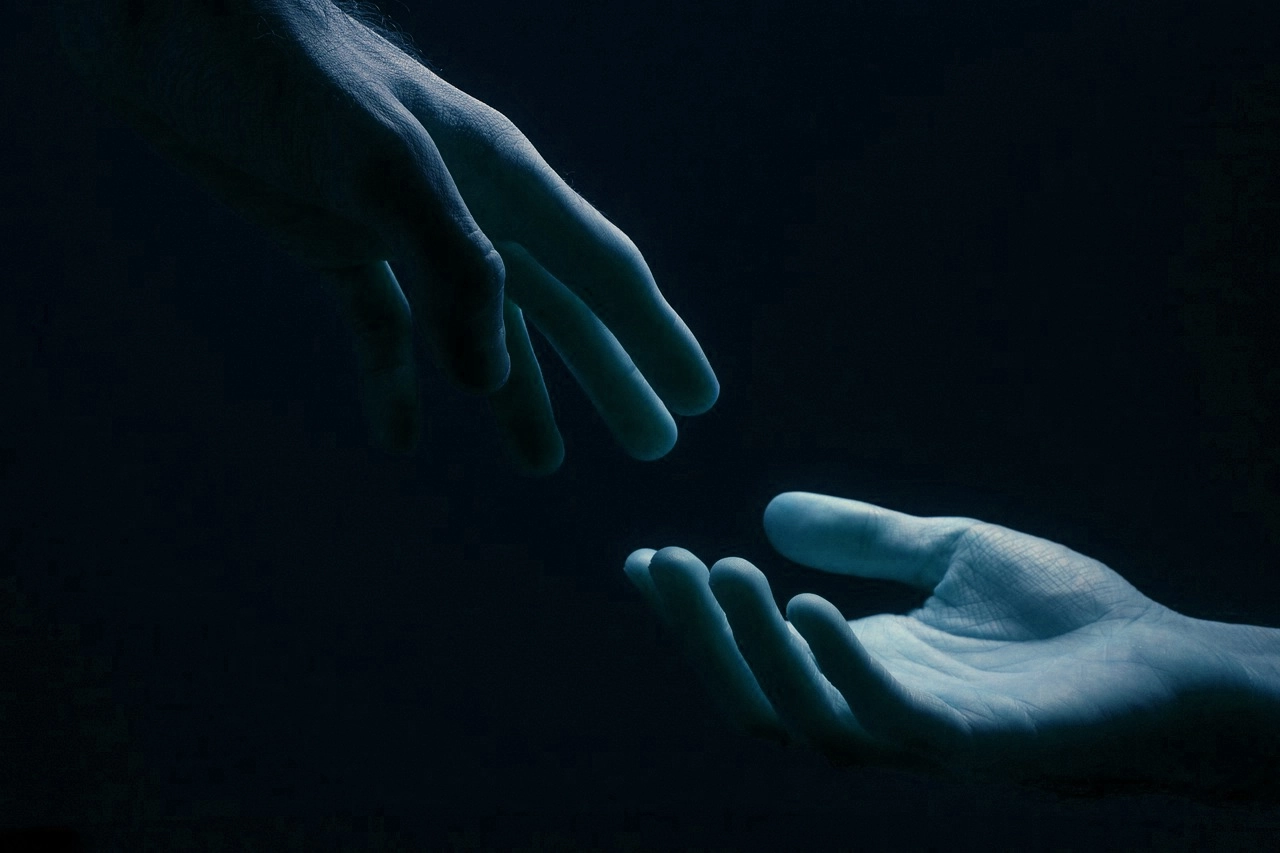 Deux mains qui se tendent l'une vers l'autre dans l'obscurité, symbole d'accompagnement, d'écoute et de soutien en hypnose, EMDR et PNL à Saint-Denis-Catus
